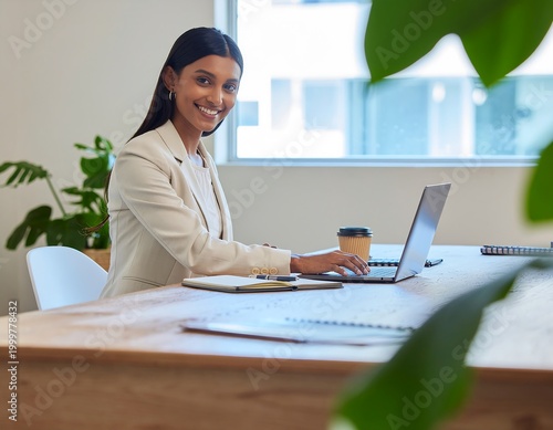 Young professional woman in a modern office setting smiling and working on a laptop, with plants in the foreground
