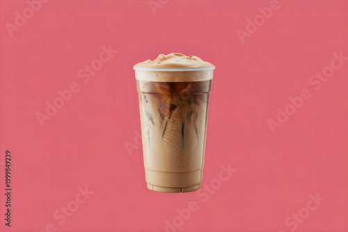 Tall plastic cup of iced coffee with creamy foam on a solid pink background