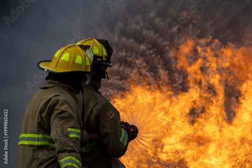 Billede på lærred Team of firefighter in fireproof clothe are using twirl fog watering hose to put