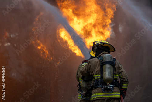Bild auf Leinwand Team of firefighter in fireproof cloth using fog watering hose to put out the bu