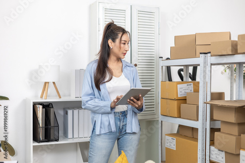 Inventory, stock, storage, warehouse, tracking, retail small business entrepreneur woman uses tablet beside parcel rack, checking products in home-based office or stockroom, keeping organized workflow