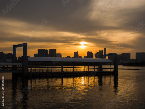 Floating water bus terminal silhouetted against a golden sunset sky at a bay park (Minato, Tokyo, Japan)