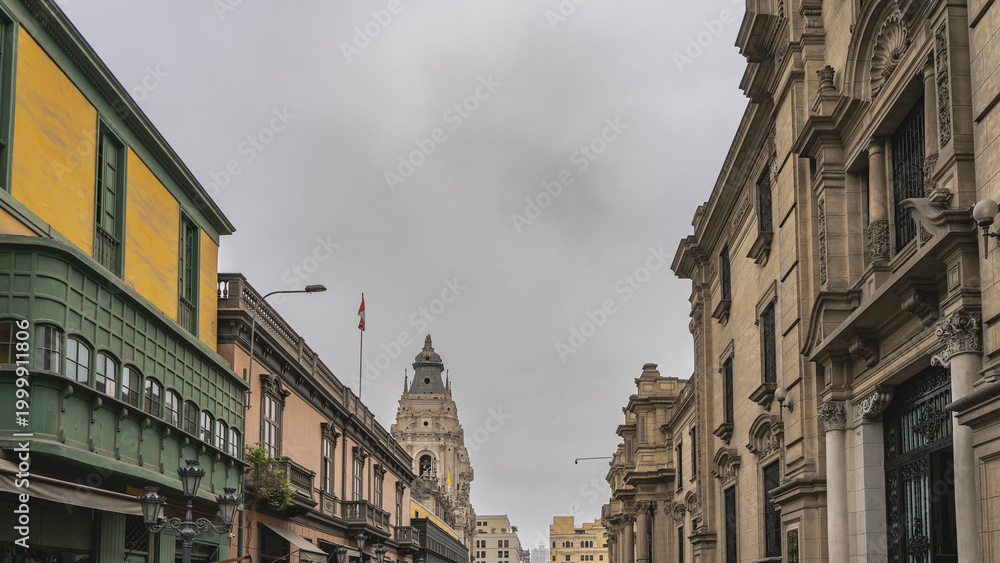 Fototapeta premium Old Spanish colonial architecture. The street of the historical quarter of Lima. Stone buildings with columns, balconies, carvings on the facades. The bell tower of the cathedral against the sky. Peru