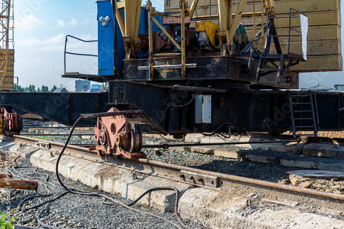 View of tower crane base with wheel mechanism on railway tracks with concrete sleepers and gravel ballast at construction site
