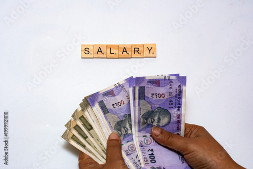 Woman counting Indian currency notes beside wooden salary blocks