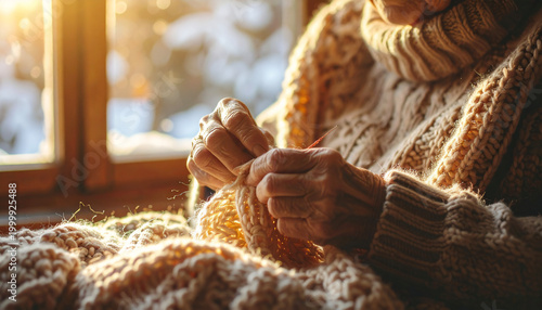 Close up of an elderly woman knitting a beige wool sweater by the window