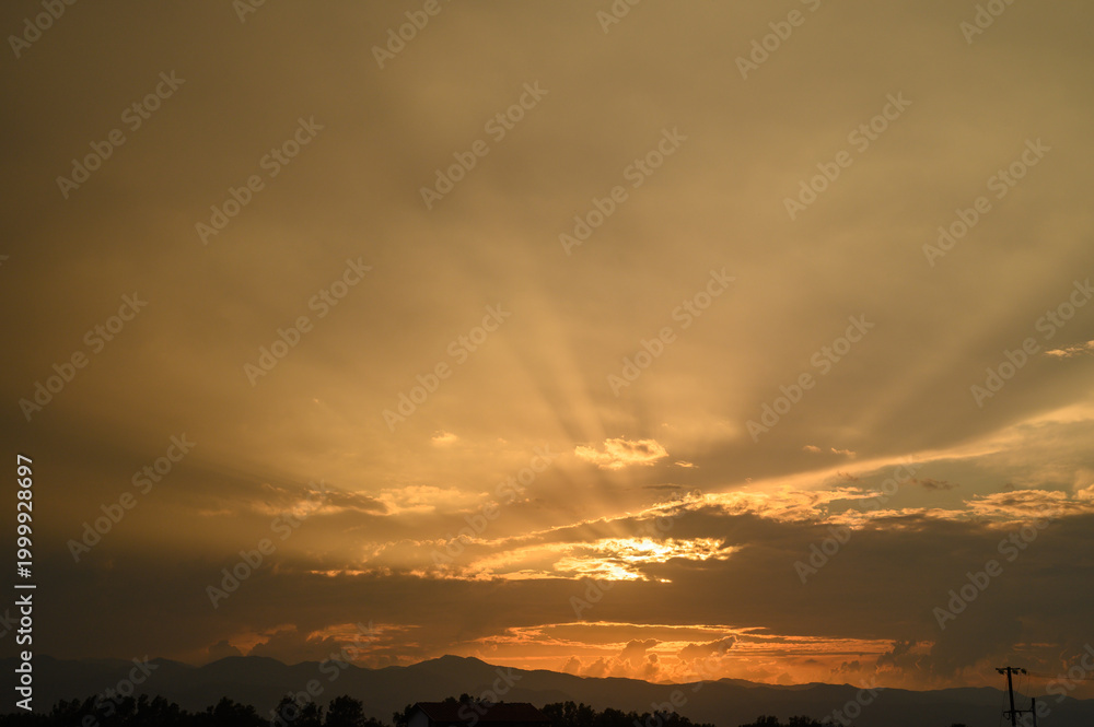 Obraz premium Golden sunset casts a warm glow over distant mountains and dramatic clouds in a tranquil evening sky