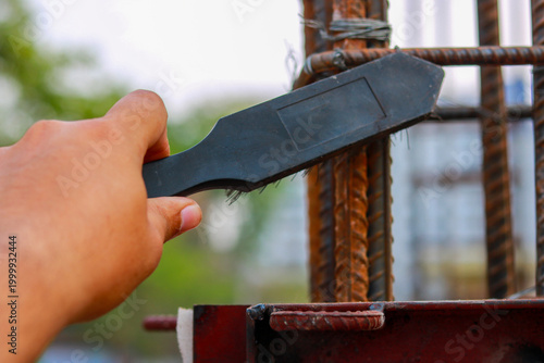 Worker Cleaning Rusty Steel Rebars with Wire Brush at Construction Site