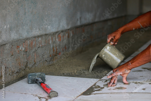 Worker pouring liquid cement mortar for floor tile installation process