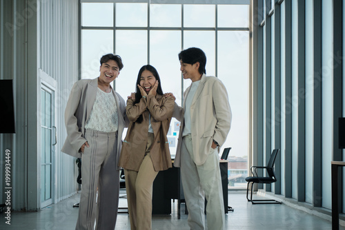 Three Asian businesspeople in a partnership team, casually standing together, in harmony and cheerful, smiling and looking at camera, business firm workers with positive motivation, corporate company.