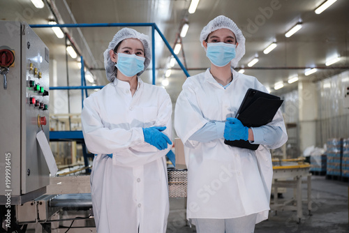 Portrait of two cheerful female industrial engineers inspecting and examining quality control production process at automated conveyor in packing manufacturing factory, quality check, and maintenance.