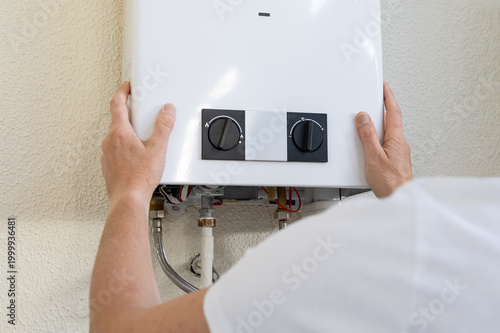 Professional plumber mounting a modern tankless gas water heater on an interior wall, hands connecting pipes and controls during residential installation and efficiency upgrade
