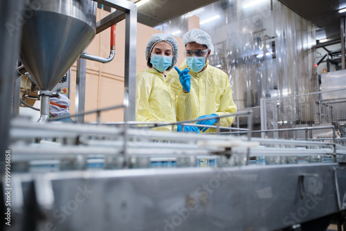 Two industrial engineer supervisors inspect and examine quality control, production process at automate conveyor in fish-canning food manufacturing factory, and protective uniforms for operations.