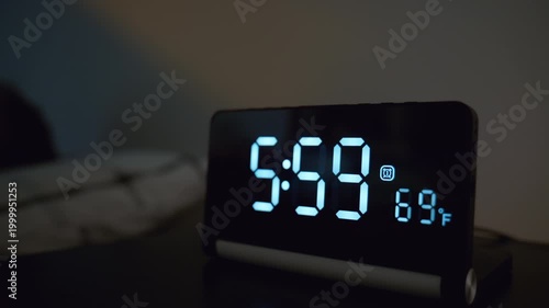 Man turning off alarm clock with his arm at 6.00 in bedroom. Early morning wake up moment with digital clock beside bed, hand reaching to stop alarm