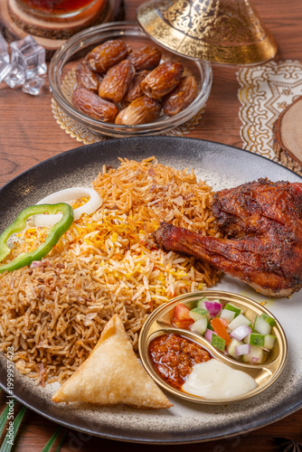 Картината върху платно nasi kebuli chicken is served on a silver plate on a wooden table served with pickles, chili sauce, and mayonnaise