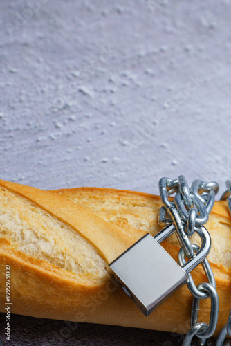 Fotografie Baguette bread wrapped with a metal chain and padlock, representing hunger, food