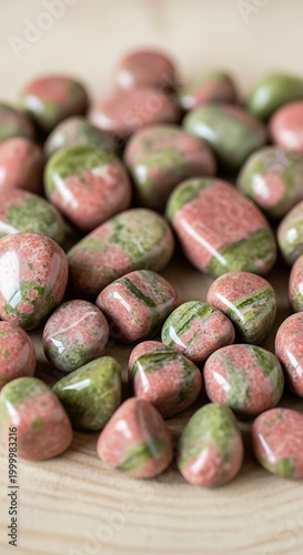 Many polished, tumbled stones display mottled pink and green coloration on a light wooden surface.
