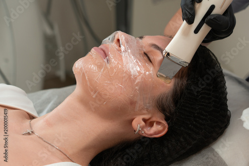 Fotografie Close up of cosmetologist performing ultrasonic facial peeling on young woman in beauty clinic