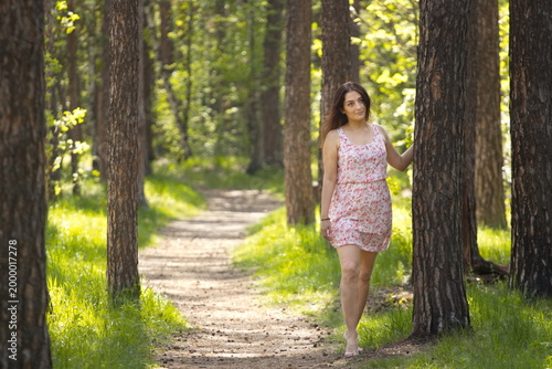 A young woman walking in the forest. An attractive woman stands barefoot near a pine tree.