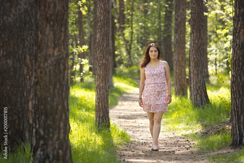 A young woman walking in the forest. A pretty woman walks barefoot along a path between pine trees.