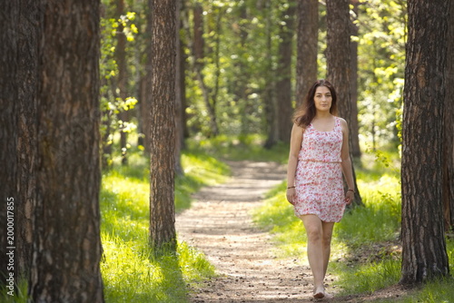 A young woman walking in the forest. A pretty woman walks barefoot along a path between pine trees.