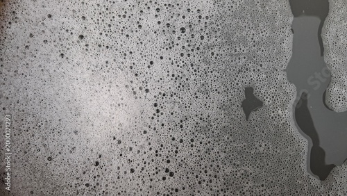 Soap foam texture with bubbles and water on gray surface.