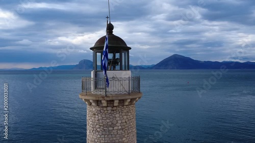 Close aerial view of stone lighthouse with Greek flag and sea horizon