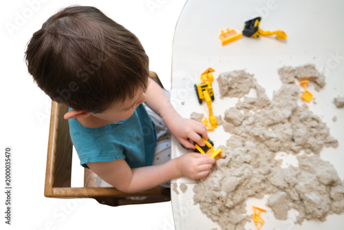 Little boy playing with kinetic sand and toy construction excavator on table. Child developing fine motor skill and sensory creativity. Early education game for preschool learning.