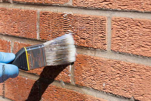 Person sealing an exterior brick wall with a clear waterproof sealant, using a paint brush. Do it yourself home improvement concept.
