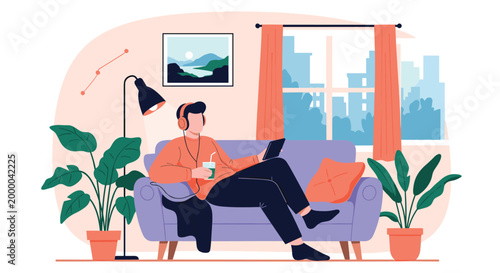 Relaxed man sits on a sofa wearing headphones and using a digital tablet while enjoying a refreshing drink in his home.