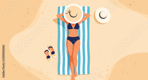 high angle view shows a woman in a dark bikini sunbathing on a blue striped towel on a sandy beach with a sun hat and flip-flops.