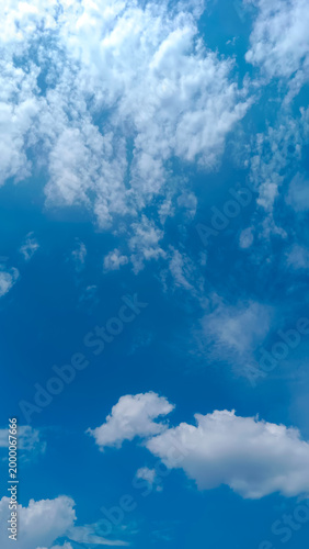 Tableau sur toile White cumulus clouds drift across a vivid blue sky in vertical composition with expansive copy space, suited for nature-themed design, wellness visuals, and mobile backgrounds