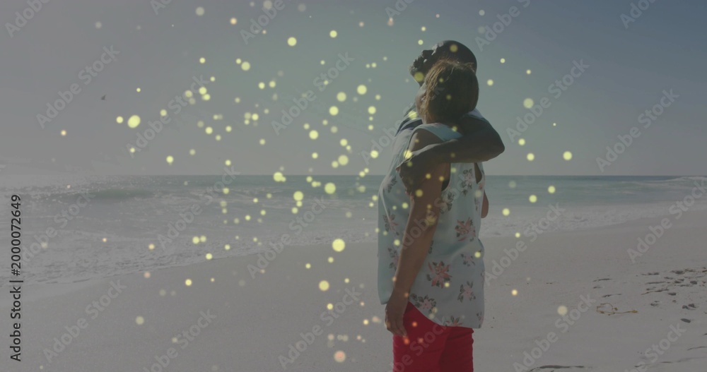 Fototapeta premium Standing couple embracing, watching ocean at beach with baseball cap, floral top, copy space