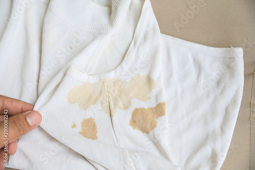 dirty yellow stains on a white rib-knit sleeveless shirt. Dirty clothes concept, sweat or food stains on fabric, laundry problem and stain removal or bleaching service background.