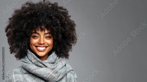 Female african young adult with natural afro hairstyle wearing a cozy plaid scarf against gray background portrait