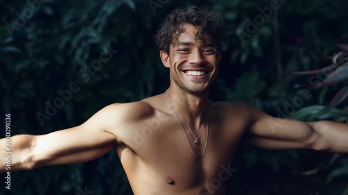 Male hispanic young shirtless tropical portrait outdoors with toned chest necklace foliage background and relaxed expression