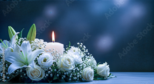 funeral condolence concept glowing candle white lilies roses floral arrangement moody dark blue background beautiful light bokeh copy space mourning sorrow grief bereavement remembrance