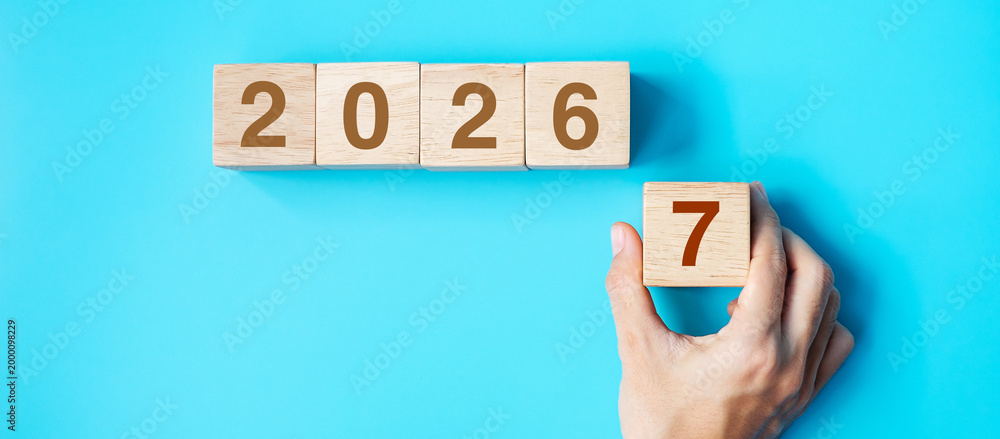 Naklejka premium hand holding wooden cube block with 2027 text on blue background. Resolution, plan, review, goal, start and New Year holiday concepts