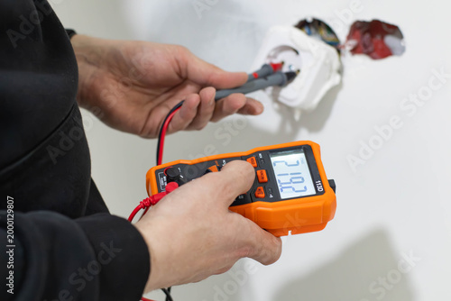 Photos Close-up of a professional technician's hands using a digital multimeter to check the voltage in a power socket during home electrical repair or maintenance