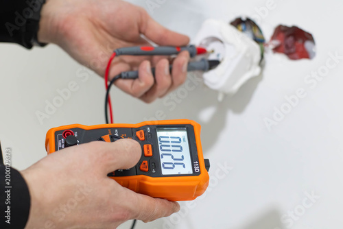 Fotografía Close-up of a professional technician's hands using a digital multimeter to check the voltage in a power socket during home electrical repair or maintenance