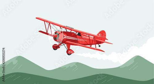 Vintage red biplane flying over green mountains with white clouds