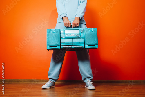 Man in blue tracksuit holding retro boombox against orange wall
