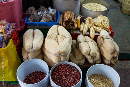 Fotografía Traditional Mexican Market Stall Displaying Tamale Packages, Fresh Corn, and Dri
