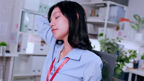 Exhausted young Asian woman employee experiencing severe neck pain taking break to stretch stiff muscles finding relief from tired tension after long hard hours of corporate overwork at office