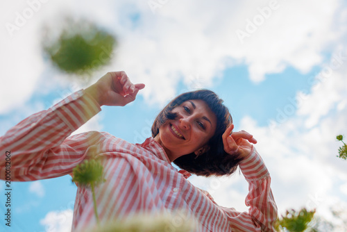 bright young girl in stylish clothes, dressed in a pink shirt, poses against a background of blue sky and flowers.