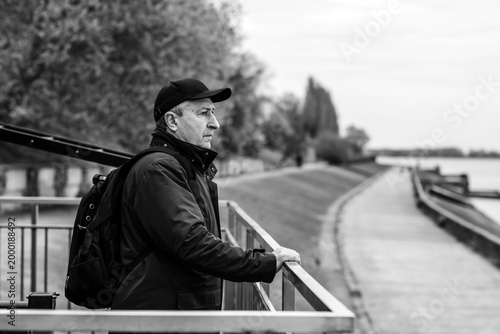 Thoughtful Mature Man with Backpack Looking at River. Active Lifestyle and Travel Concept