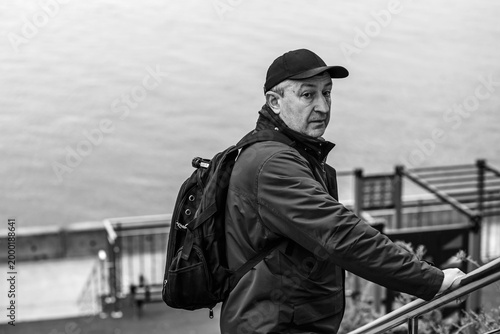 Thoughtful Mature Man with Backpack Looking at River. Active Lifestyle and Travel Concept