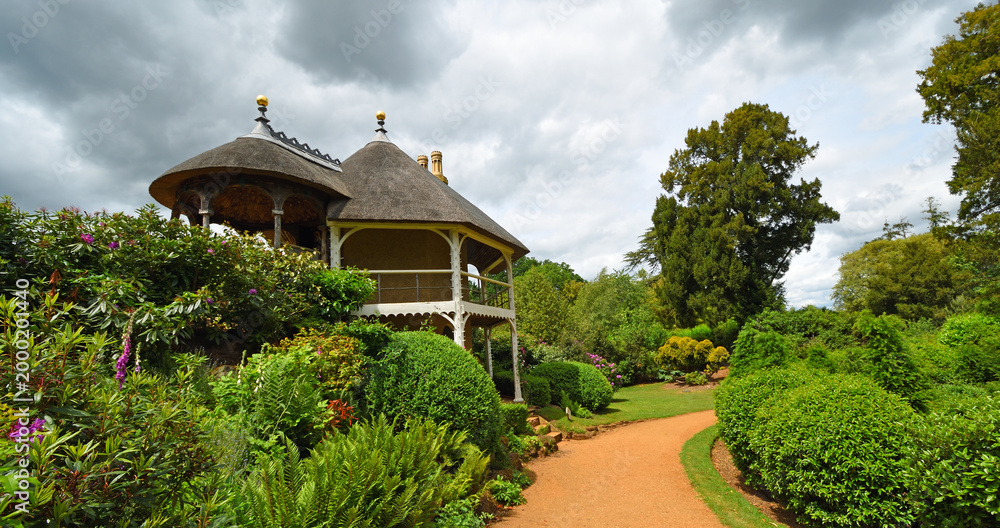 Obraz na plátně Garden with Swiss tyle summer house large shrubs and trees