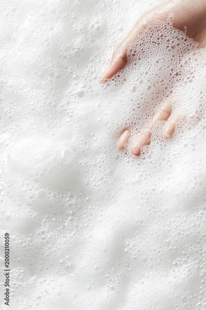 Fototapeta premium Hand submerged in white sudsy water with many small bubbles, close-up view.