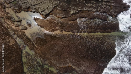 Aerial shot of the ocean with waves doing swirls and patters, rocks, sand and beach